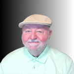 An older man with a white beard and mustache, wearing a beige flat cap and a light green collared shirt, smiles in front of a black-to-white gradient background.