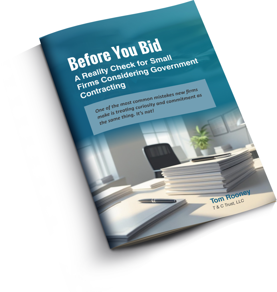Angled view of a booklet titled "Before You Bid: A Reality Check for Small Firms Considering Government Contracting" by Tom Rooney, featuring an office desk with papers, pens, and a chair in the background.